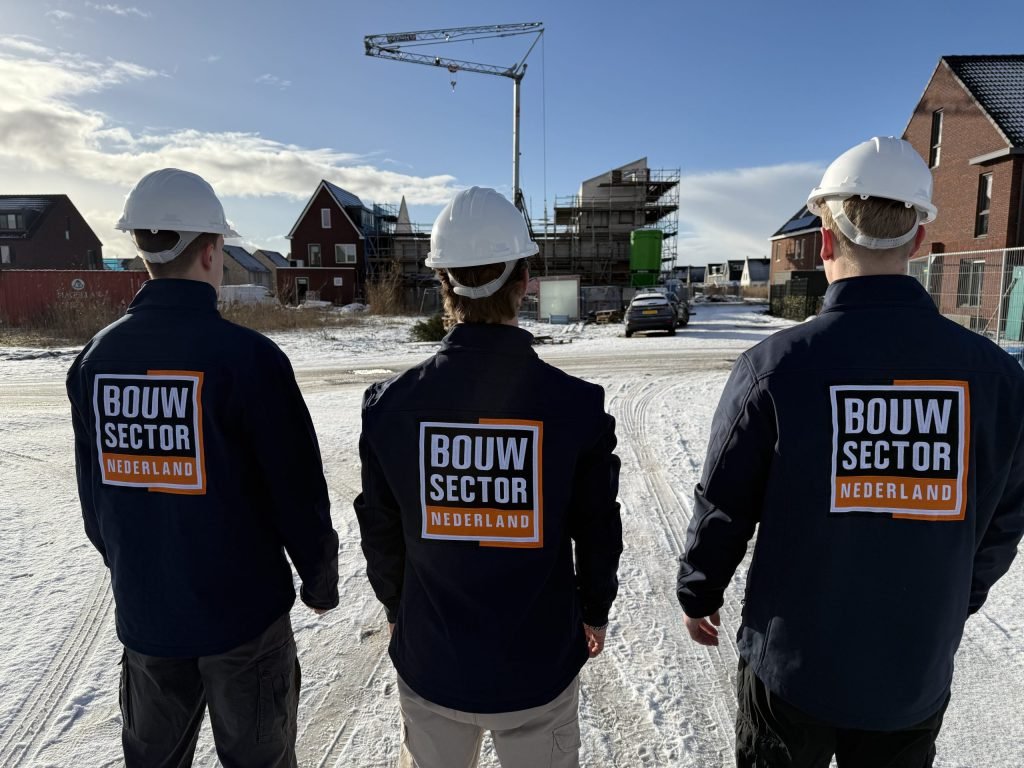 Drie vakmensen van Bouwsector Nederland in werkjassen met logo kijken naar nieuwe woningen in aanbouw
